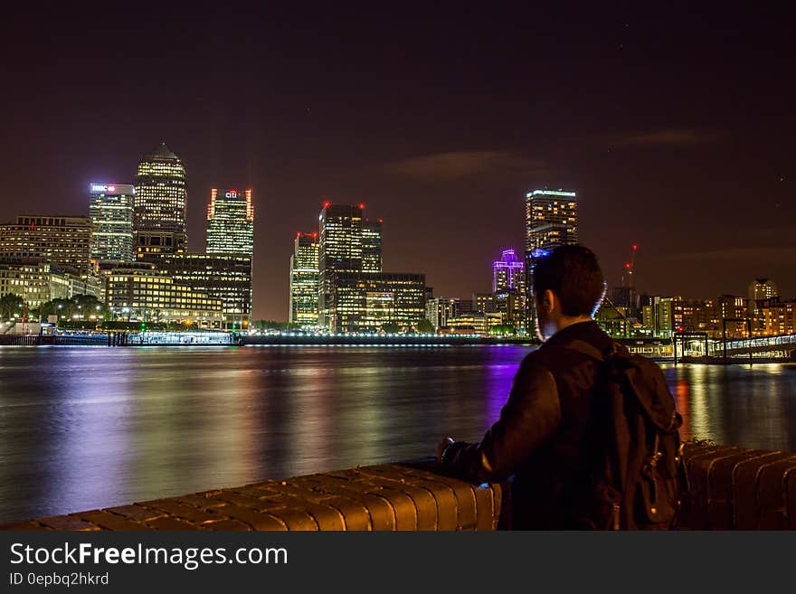 Man standing on banks of River Thames overlooking London, England skyline illuminated at night. Man standing on banks of River Thames overlooking London, England skyline illuminated at night.