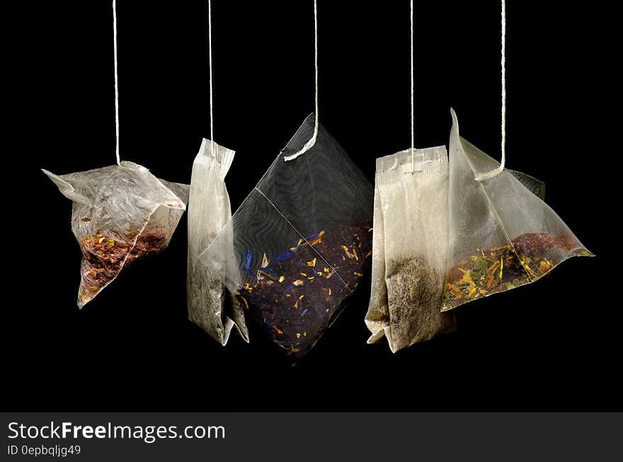 Close up on variety of tea bags hanging against white background.