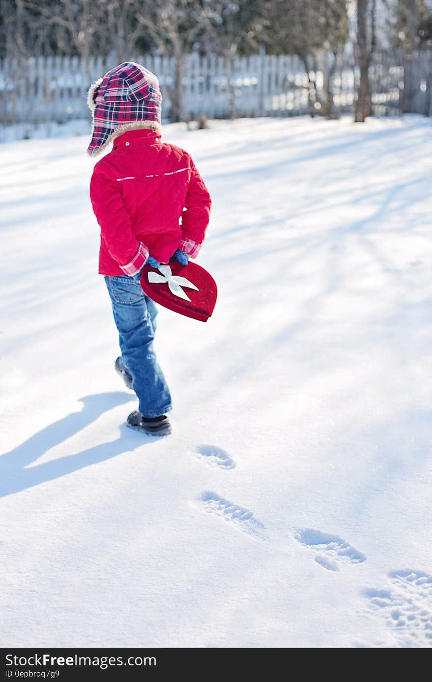 Child carrying heart shaped chocolate box through snowy field. Child carrying heart shaped chocolate box through snowy field.