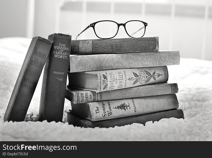 Stack of books on bed with eyeglasses in black and white. Stack of books on bed with eyeglasses in black and white.