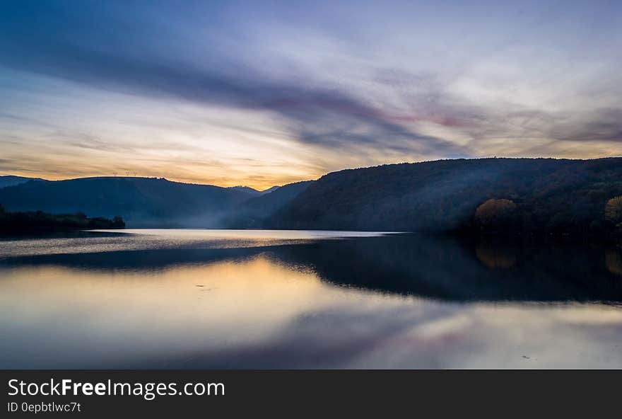 Sunset behind hillside of lakefront landscape with cloudy skies. Sunset behind hillside of lakefront landscape with cloudy skies.