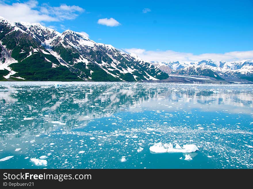 Mountain Filled With Snow Near Calm Sea Under White Clouds and Blue Sky during Daytime