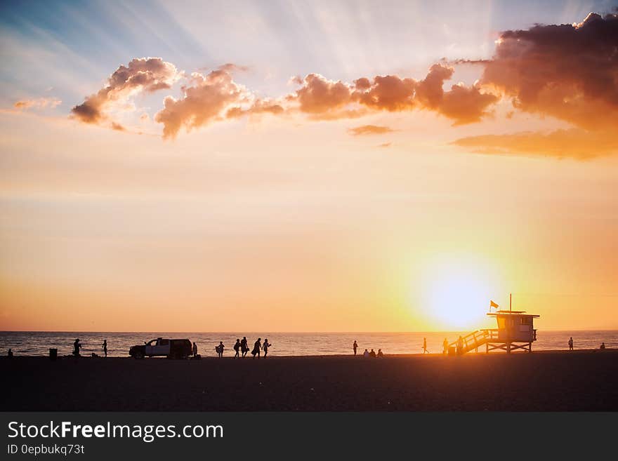 Silhouette of lifeguard shack and people on beach at sunset.