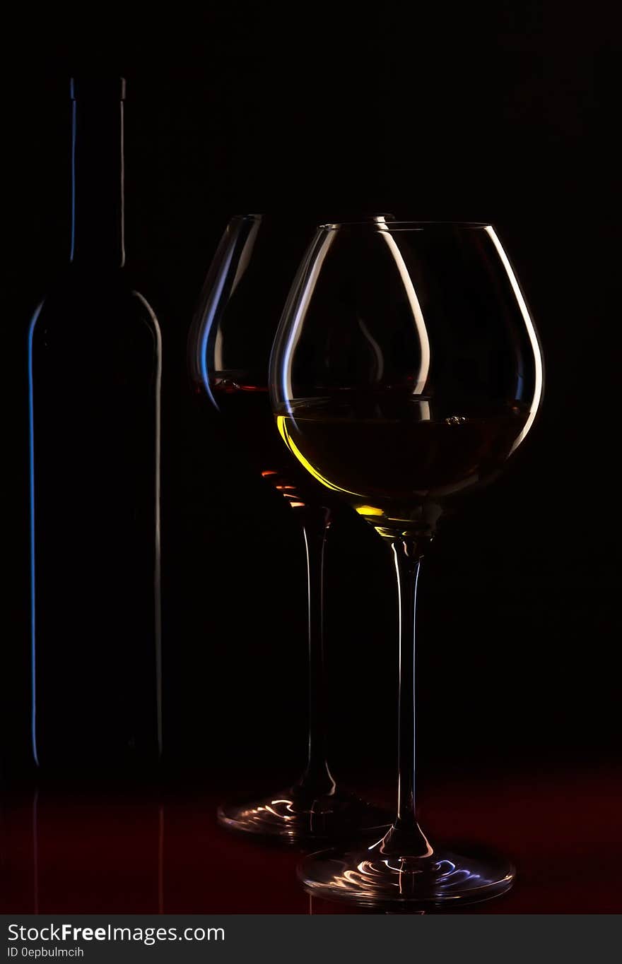 Stemmed wineglasses with red and white wine and bottle on black background. Stemmed wineglasses with red and white wine and bottle on black background.