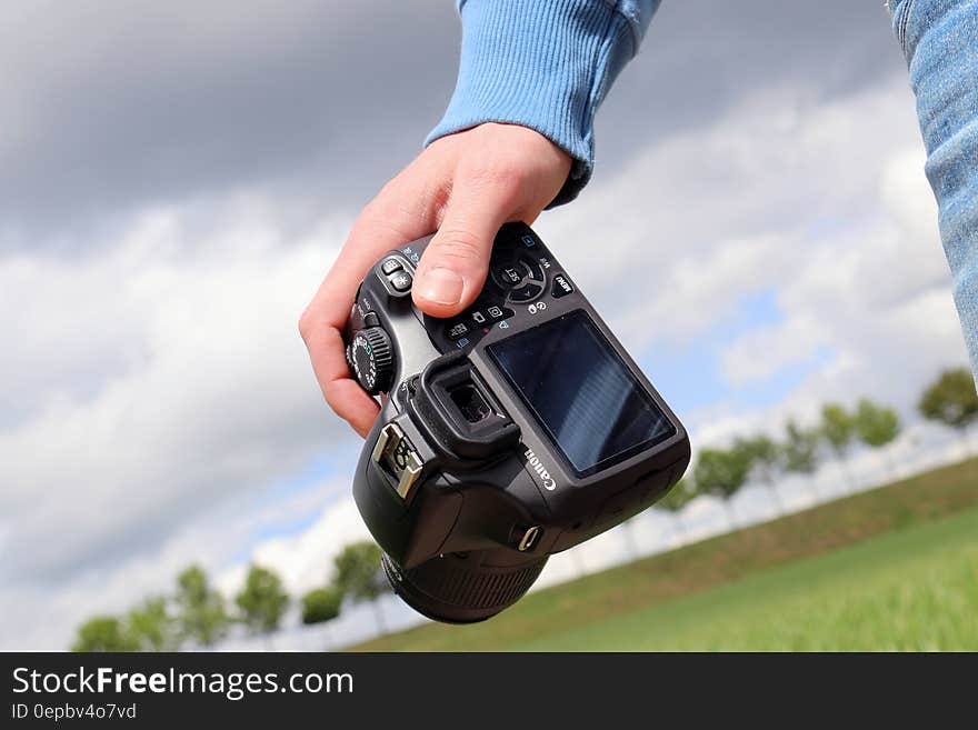 Hand of person carrying digital camera in countryside with field, trees and sky in background. Hand of person carrying digital camera in countryside with field, trees and sky in background.