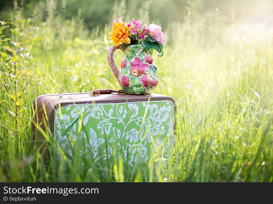 Vase of flowers on decorative suitcase in field of long grass with summer sunlight. Vase of flowers on decorative suitcase in field of long grass with summer sunlight.