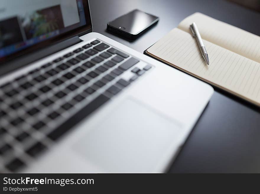 A close up of a laptop computer and a notebook with mobile phone. A close up of a laptop computer and a notebook with mobile phone.