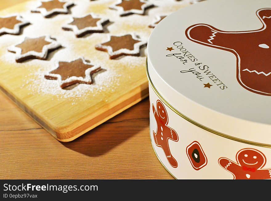 Tin marked "Cookies and Sweets for you" decorated with brown gingerbread men and beside it on a wooden board five star biscuits on a sprinkling of flour ready for baking in the oven. Tin marked "Cookies and Sweets for you" decorated with brown gingerbread men and beside it on a wooden board five star biscuits on a sprinkling of flour ready for baking in the oven.