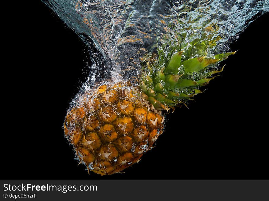 Whole fresh pineapple splashing into water against black background. Whole fresh pineapple splashing into water against black background.