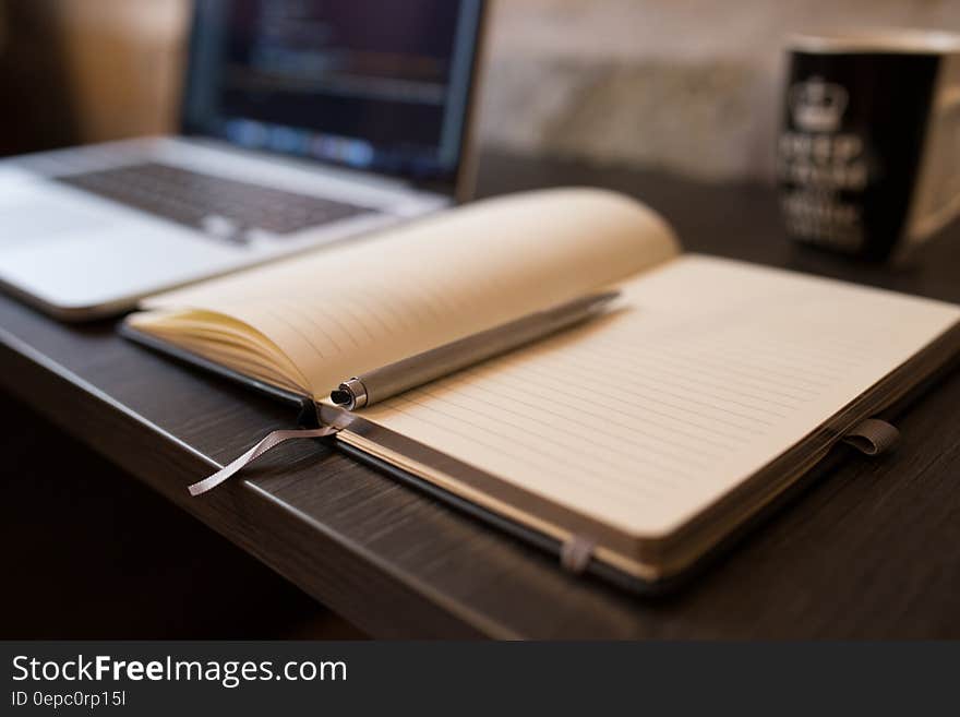 Open blank notebook and pen next to laptop computer on desk. Open blank notebook and pen next to laptop computer on desk.