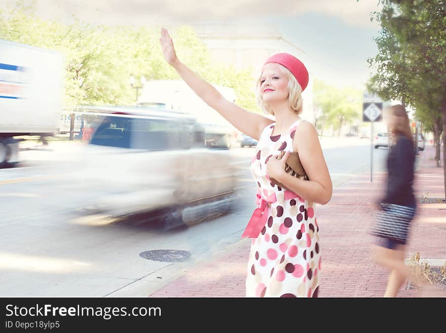 Fashionable young woman on sidewalk hailing taxi cab from road with traffic motion blur. Fashionable young woman on sidewalk hailing taxi cab from road with traffic motion blur.