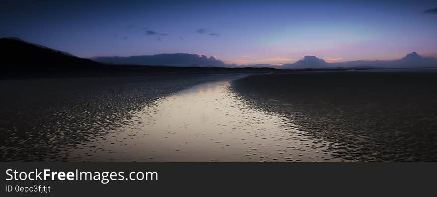 Sunset over country lake with pink and blue skies and mountain peaks.