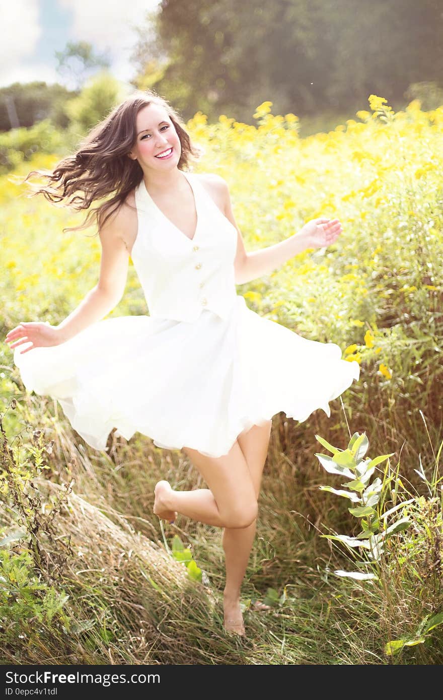 Sunny portrait of long brunette in white dress running barefoot through grassy field. Sunny portrait of long brunette in white dress running barefoot through grassy field.