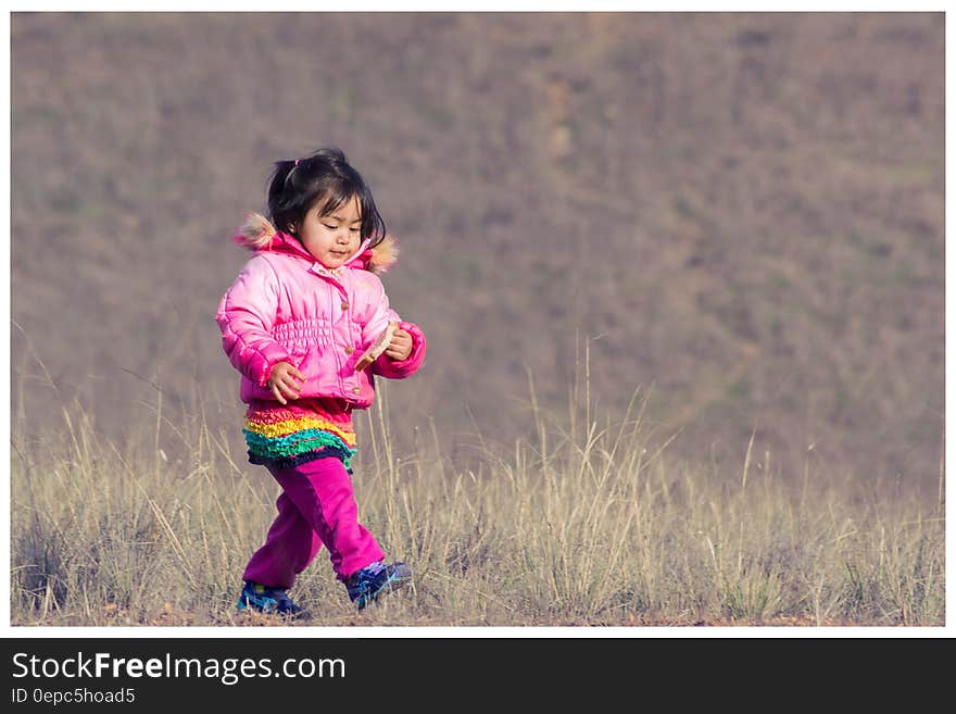 Woman in Pink Down Jacket Walking on Green Grass during Daytime