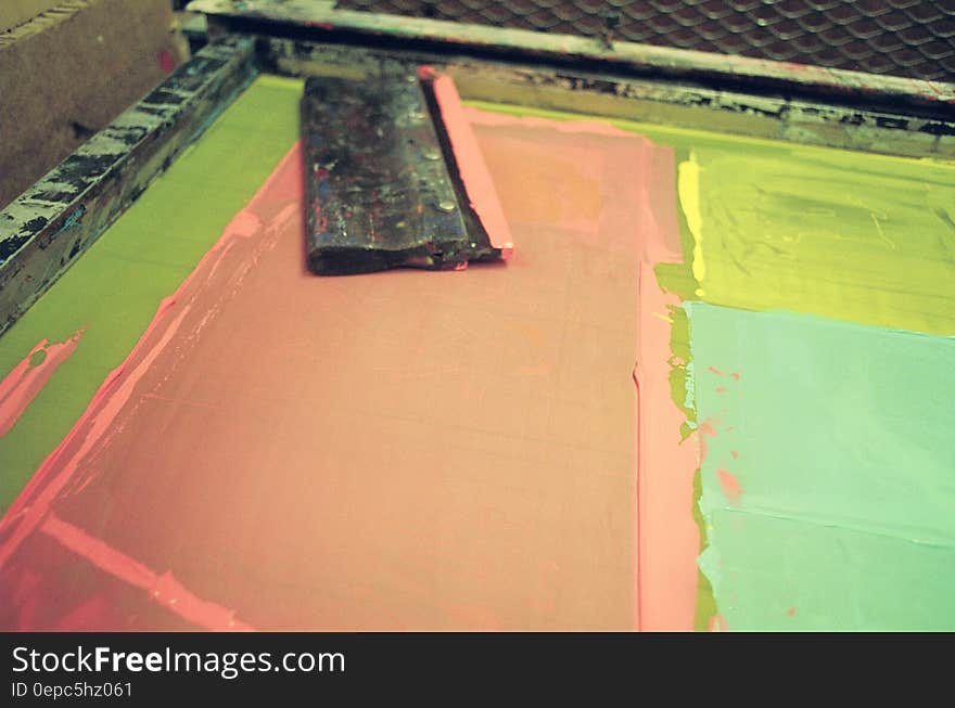 Table with black wooden squeegee and three colors pink yellow and green for generating artistic screen prints in combinations of these colors, studio background. Table with black wooden squeegee and three colors pink yellow and green for generating artistic screen prints in combinations of these colors, studio background.