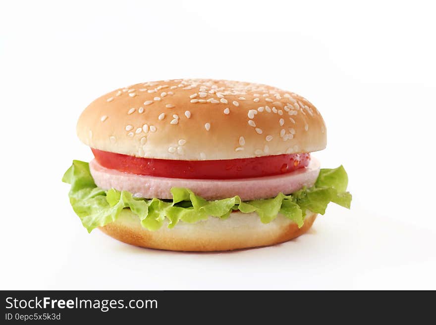 Tasty cheeseburger in a seeded bun with tomato, lettuce, plus cheese and ham, white background.