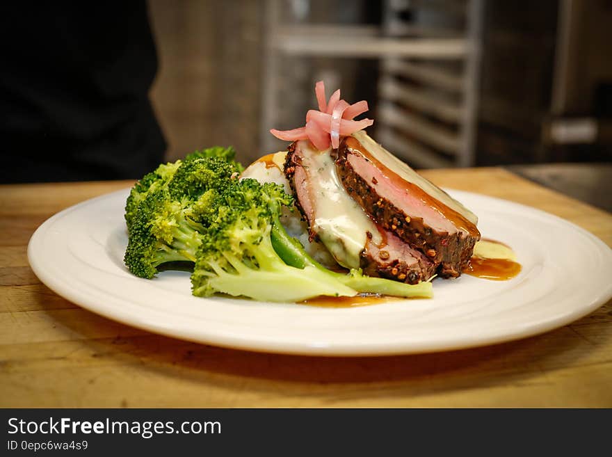 A portion of steaks with broccoli on a wooden table.