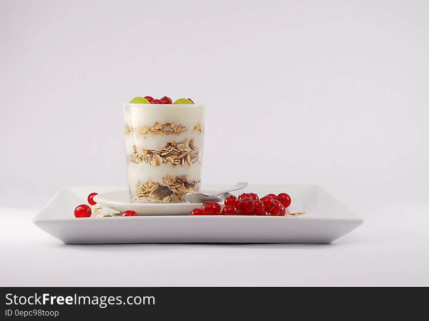 A layered breakfast with yogurt, cereals and berries and fruits in a glass on a rectangular plate.