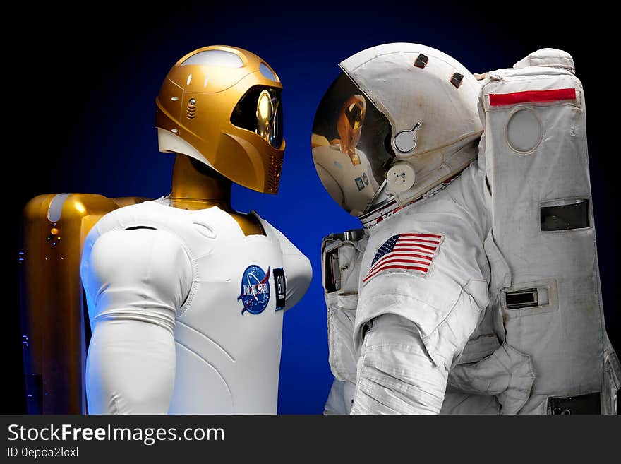 Human and robotic astronauts stood facing each other with different style equipment.