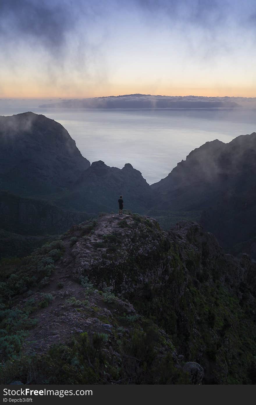 A lone hiker standing on a mountain top enjoying the view of the sea at dusk. A lone hiker standing on a mountain top enjoying the view of the sea at dusk.