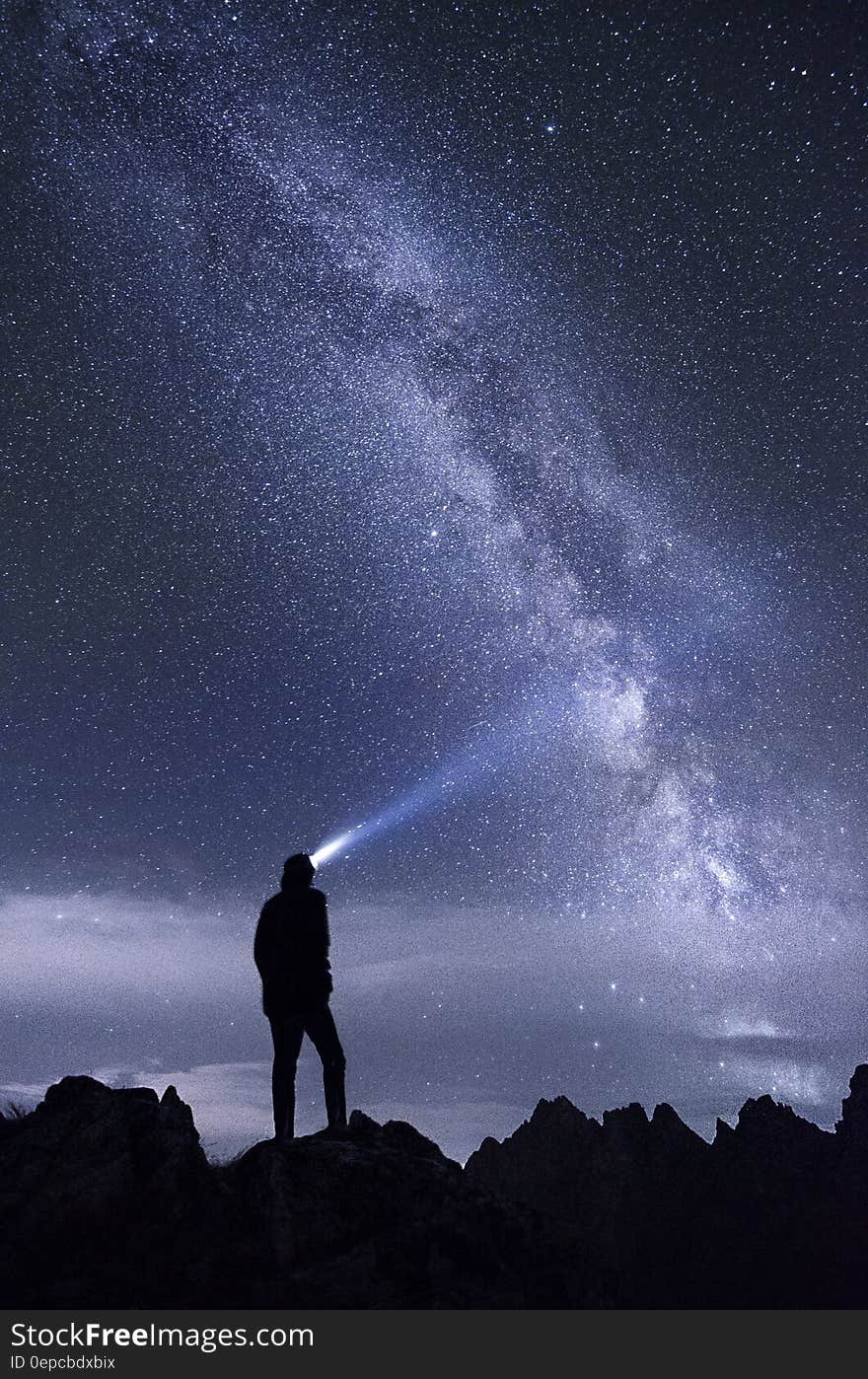 A silhouette of a man looking at the Milky Way in the night sky above him.