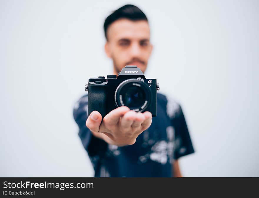 Young man holding a digital camera on palm on hand, focus on camera and white studio background.