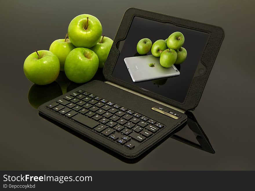 A black laptop with apple desktop background and green apples beside it. A black laptop with apple desktop background and green apples beside it.