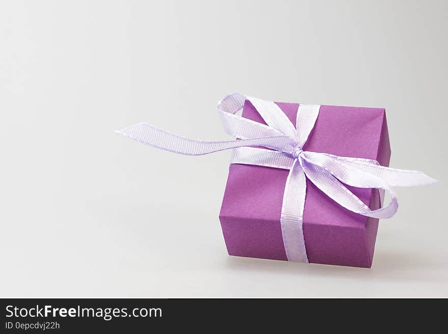 Square shaped present wrapped in purple paper with decorative ribbon, white studio background with copy space. Square shaped present wrapped in purple paper with decorative ribbon, white studio background with copy space.