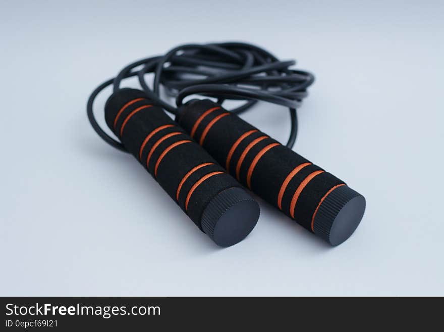 A jump rope with black handles with orange stripes.