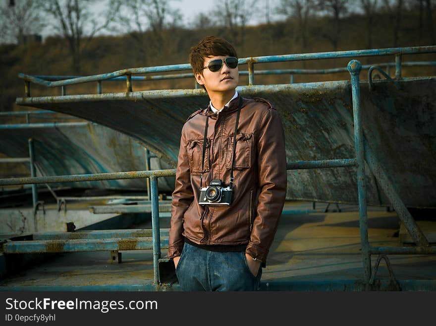 Outdoor portrait of man standing in leather jacket with camera around neck wearing sunglasses. Outdoor portrait of man standing in leather jacket with camera around neck wearing sunglasses.