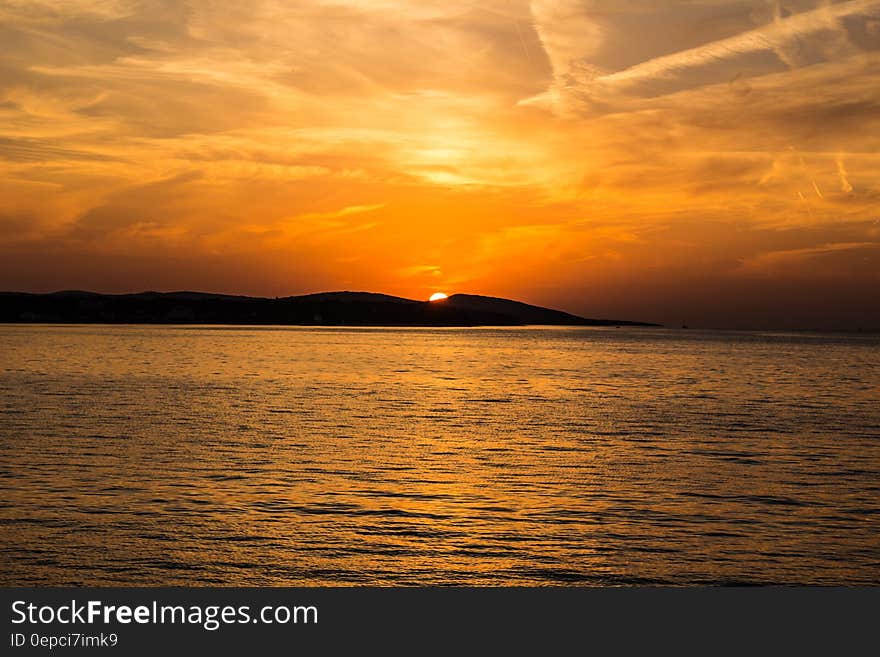 A sunset on the sea with an island in the horizon.