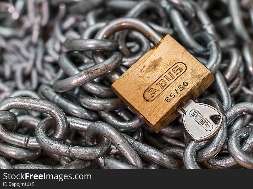 Brass padlock and key with selective focus and steel chain creating a background concept of security. Brass padlock and key with selective focus and steel chain creating a background concept of security.