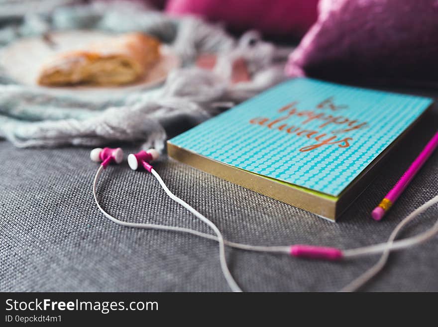 White and Pink Earphones on Gray Textile