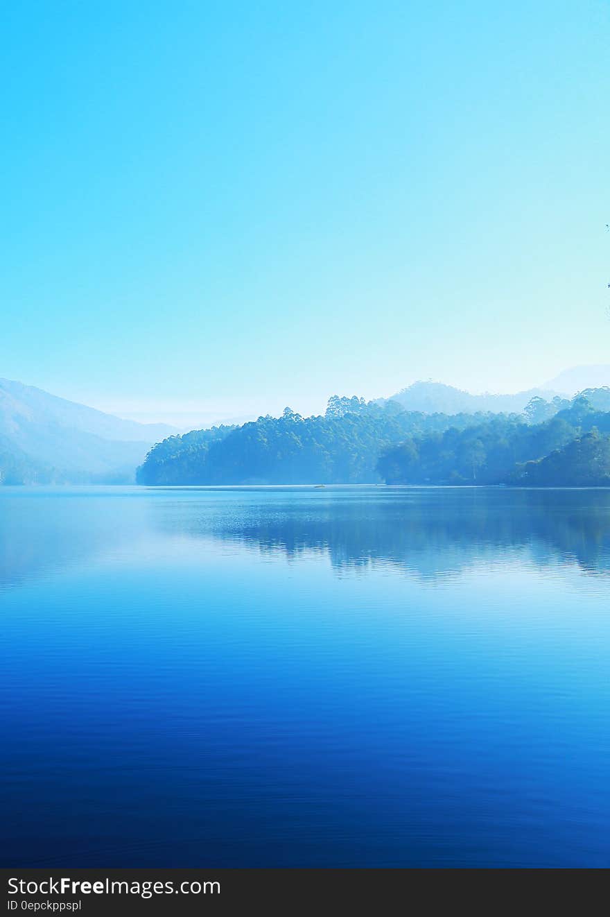 Blue lake with misty shores and clear skies above.