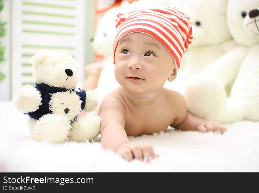 Smiling Toddler Wearing Orange and White Knit Cap Beside Black and White Bear Plush Toy