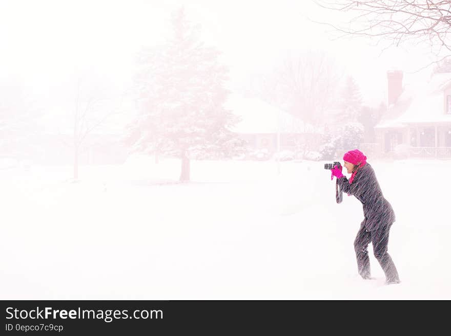 Woman in Pink Hijab Holding Black Dslr Camera Under Raging Snow during Daytime