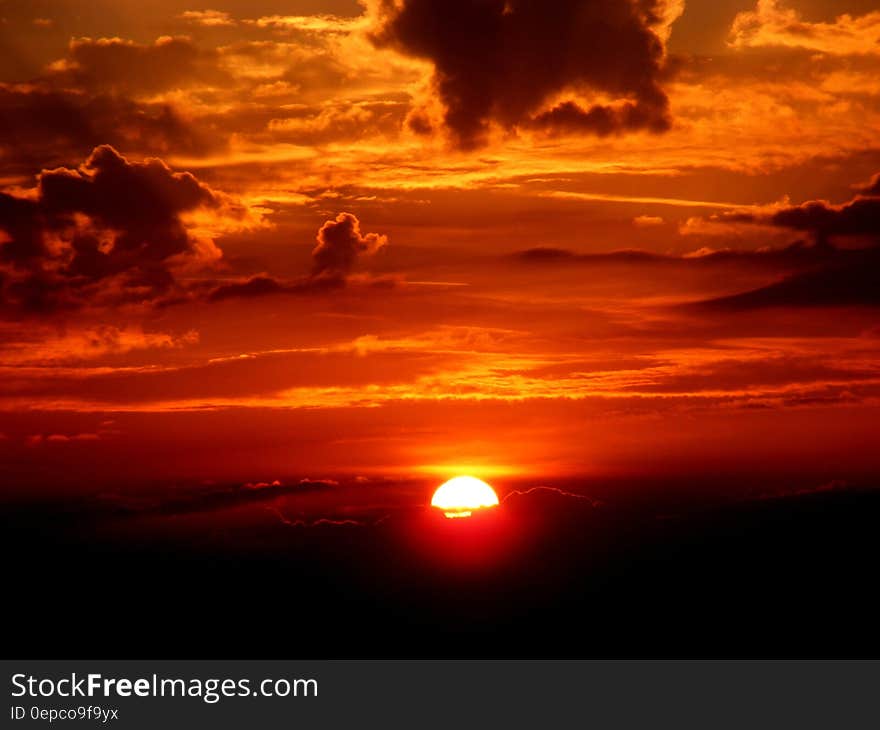 Sun setting over horizon in cloudy orange skies. Sun setting over horizon in cloudy orange skies.