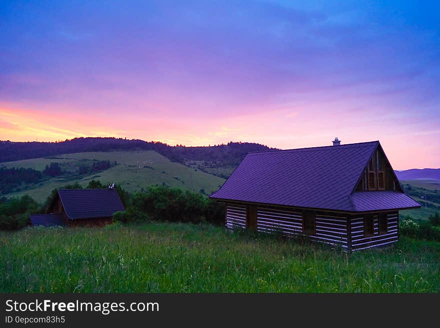 Wooden cottage in green field on hillside at sunset. Wooden cottage in green field on hillside at sunset.