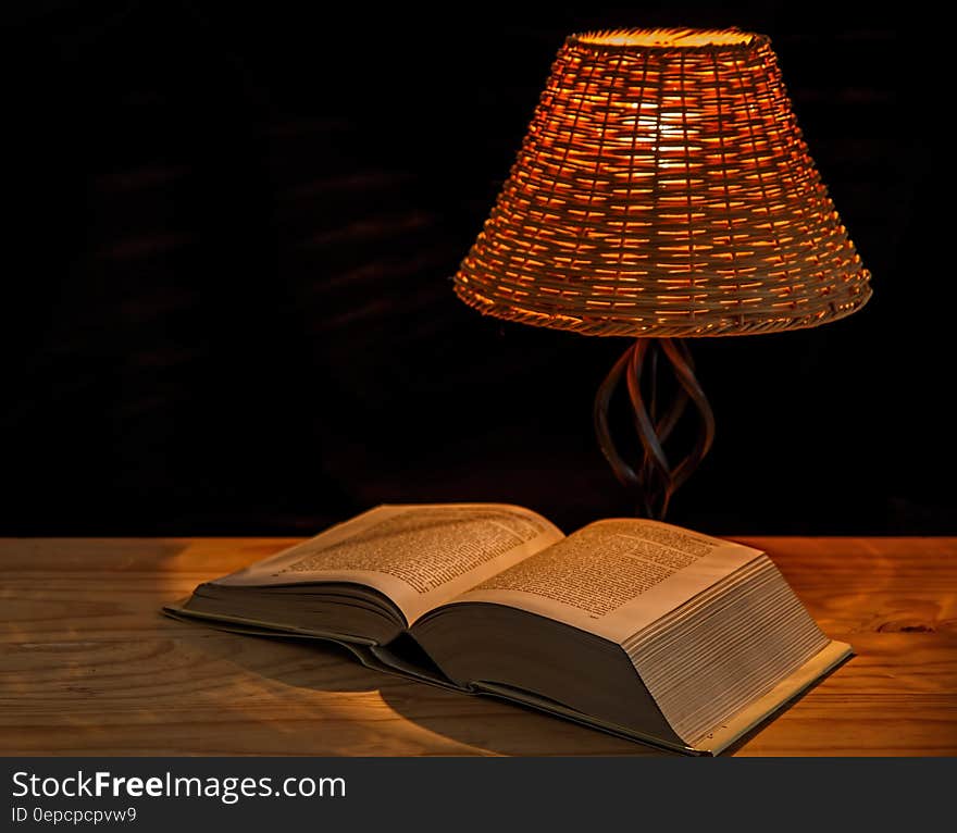 Open encyclopedia on wooden table under lamp with black background and copy space. Open encyclopedia on wooden table under lamp with black background and copy space.