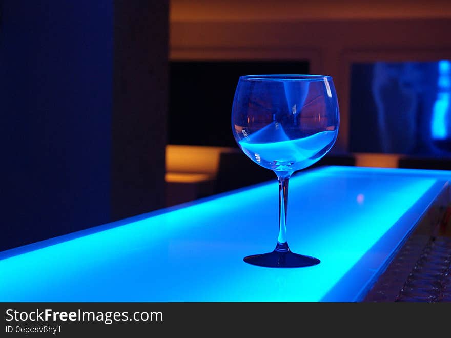 Stemmed glass on counter with blue light inside bar. Stemmed glass on counter with blue light inside bar.