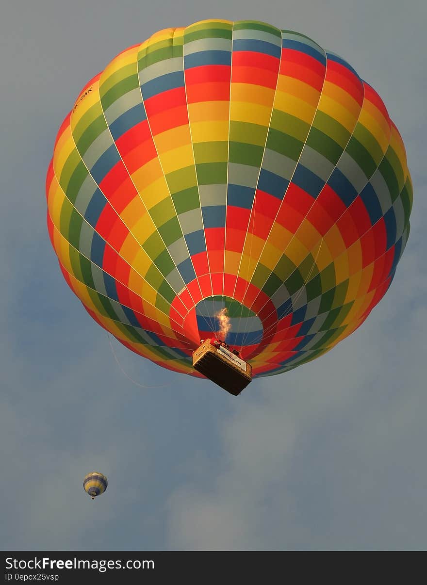 Colorful hot air balloon with basket against blue skies and white clouds.