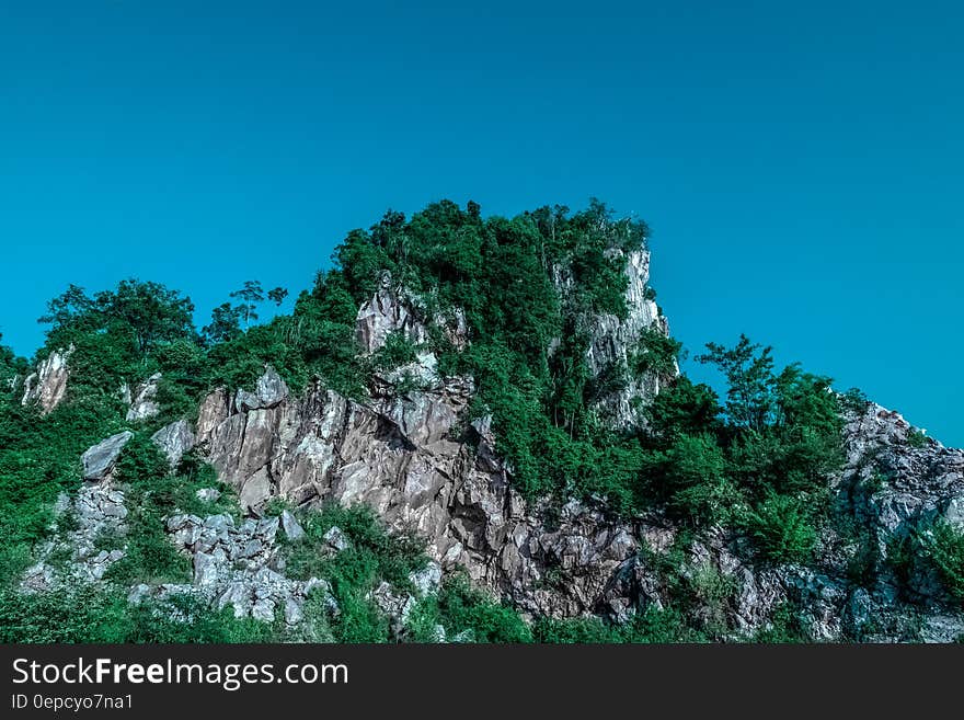 Tree covered rocky crag against blue skies on sunny day.