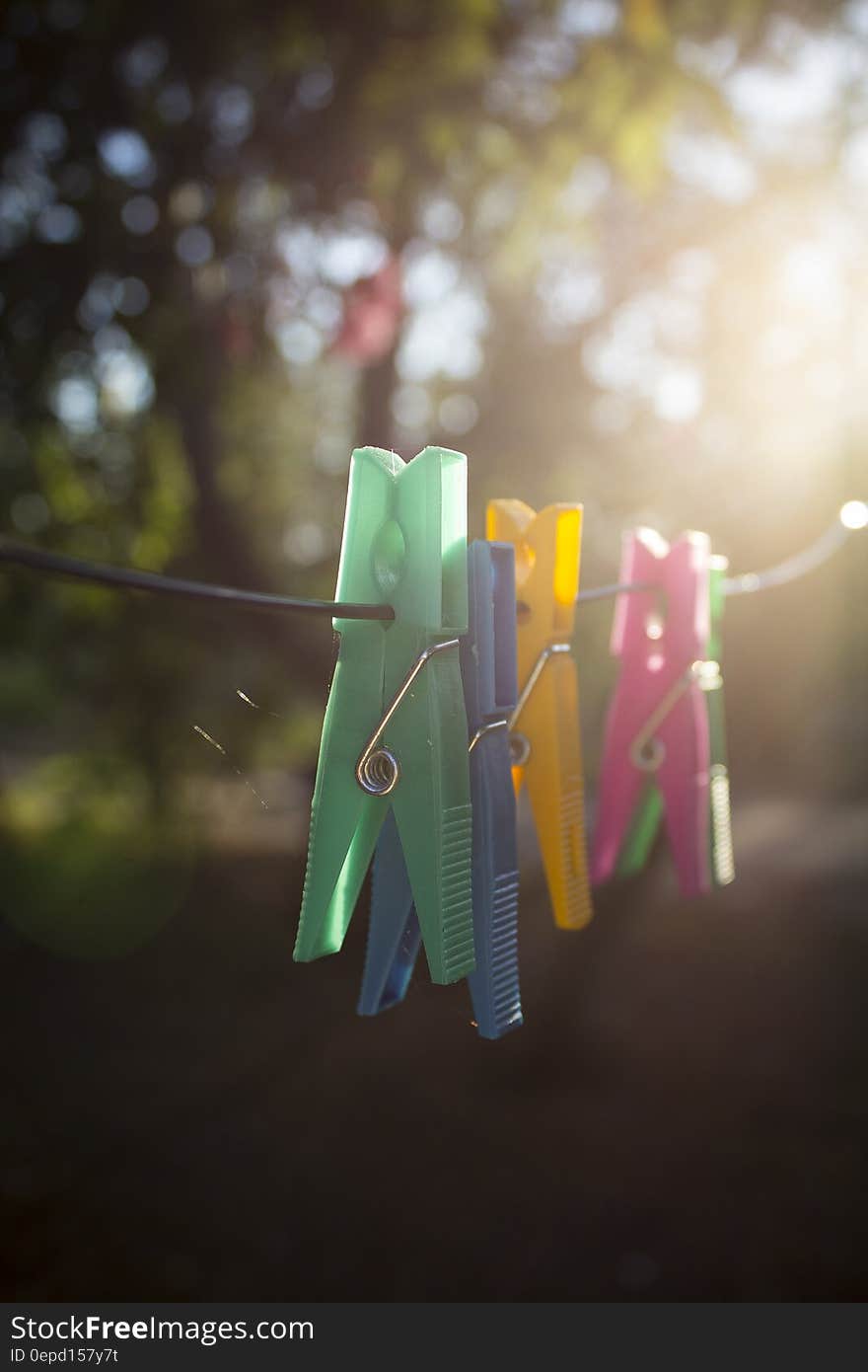 Closeup of green, blue, yellow and pink clothes pegs on a washing line with sunshine streaming through the trees in the background. Closeup of green, blue, yellow and pink clothes pegs on a washing line with sunshine streaming through the trees in the background.