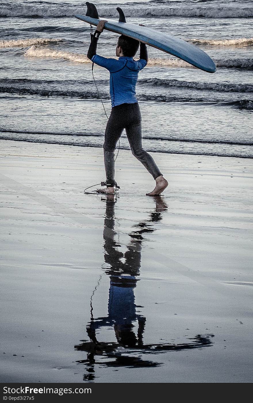 Young boy carrying surfboard along beach. Young boy carrying surfboard along beach.