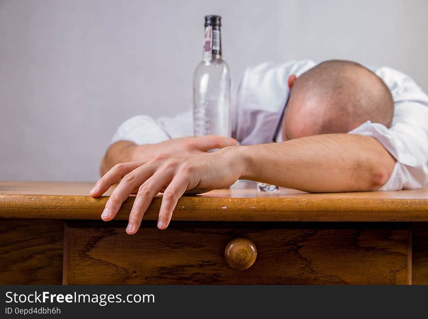 Man in White Dress Shirt Holding Glass Bottle on Brown Wooden Table