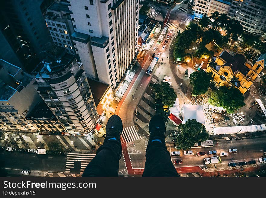 Man Sitting on High Rise Building Taking Photo Below