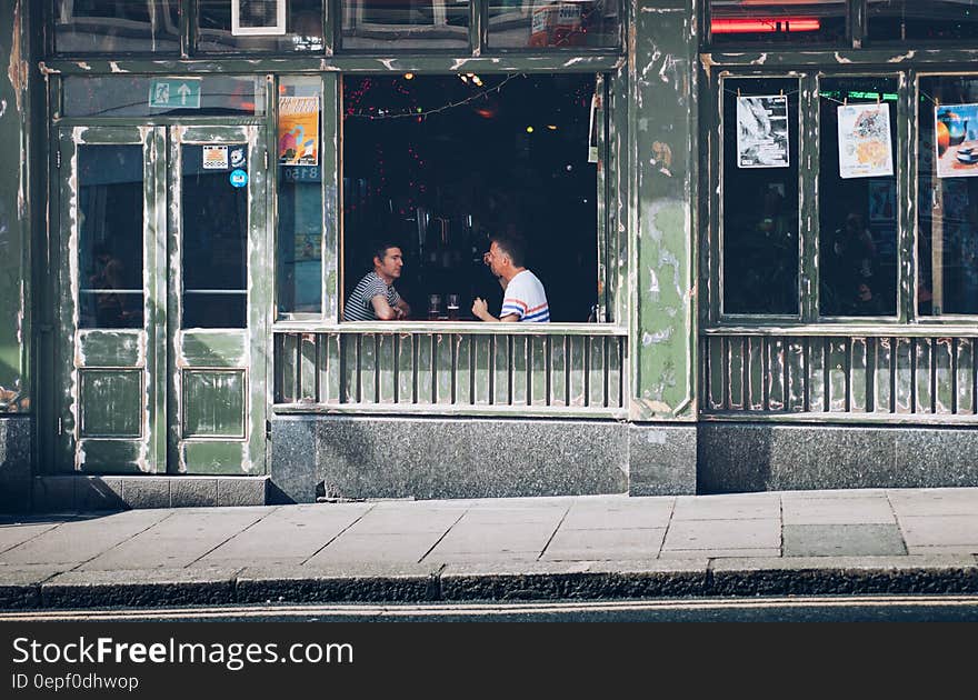 Two Men Eating While Facing Each Other Inside Store