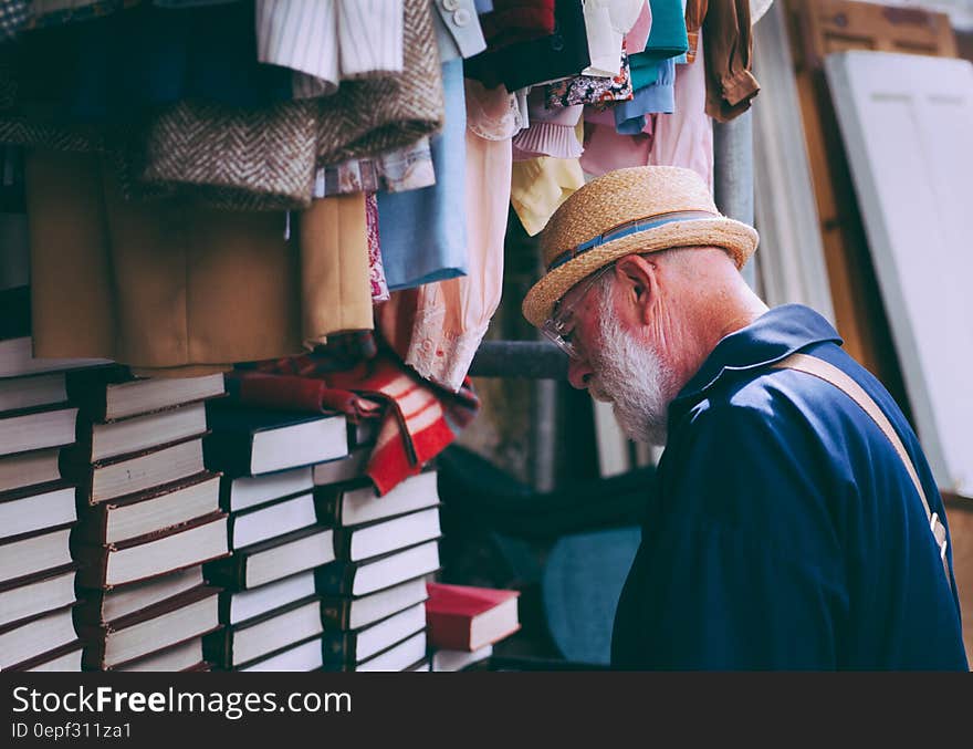 Man in Brown Sun Hat Facing Black Covered Piled Books