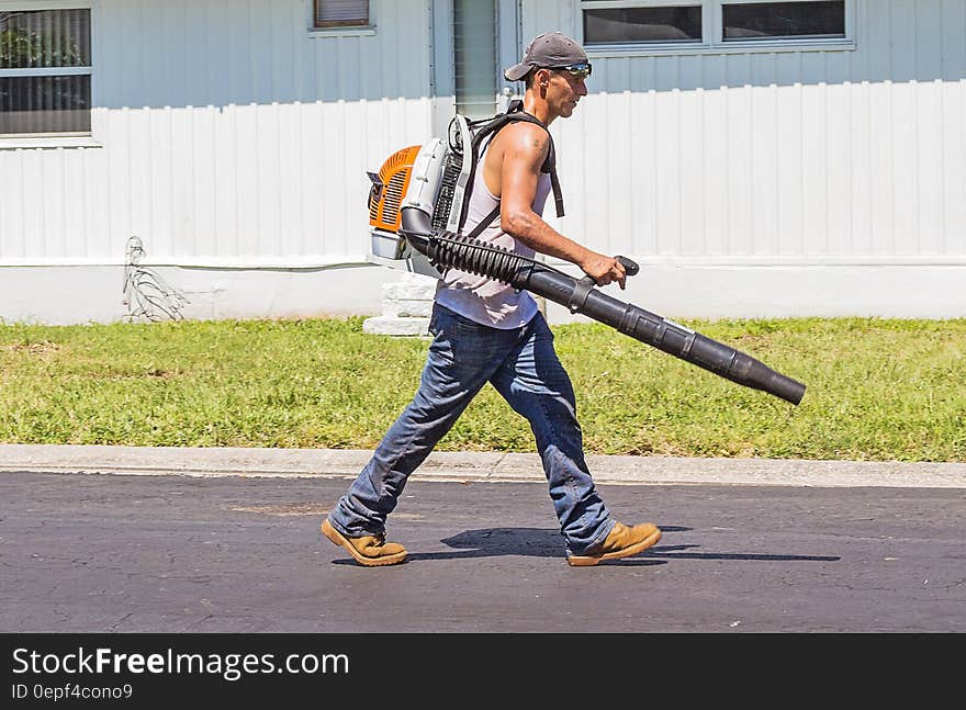 Man in White Tank Top and Blue Denim Pants With Leaf Blower Outdoors during Daytime