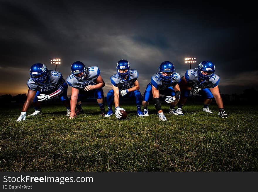 Football Players in Blue Jersey Lined Under Grey White Cloudy Sky during Sunset